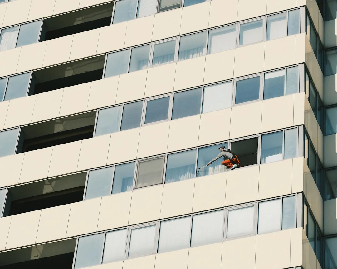 Trois nettoyeurs de vitres suspendus à des cordes nettoient la façade vitrée d’un immeuble moderne en journée.
